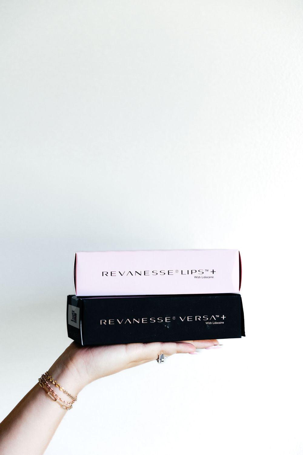 Multiple hands holding up Revanesse Versa dermal filler product boxes against a white background.