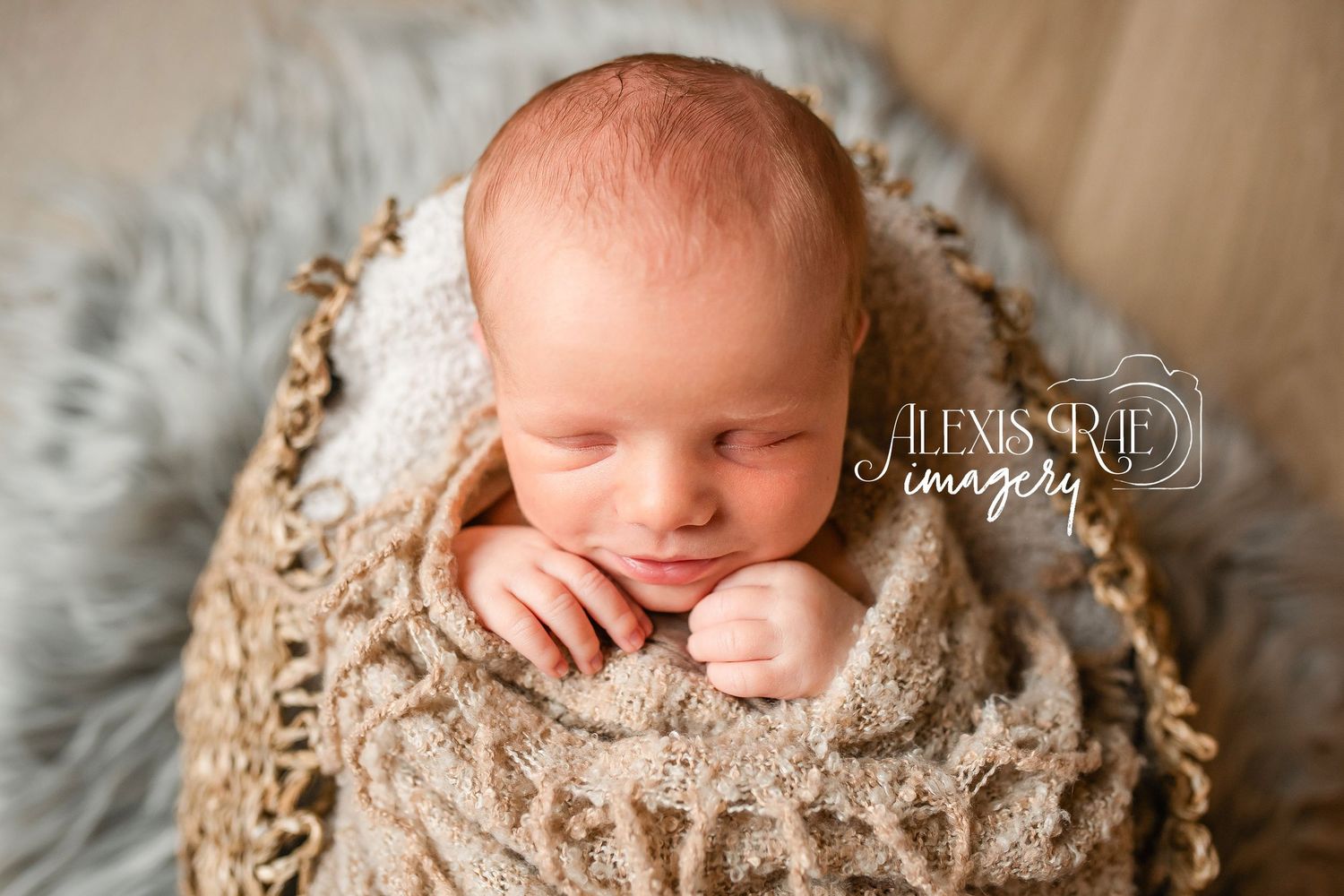 Peaceful sleeping newborn wrapped in cozy beige knit blanket on soft gray backdrop during professional photo session.
