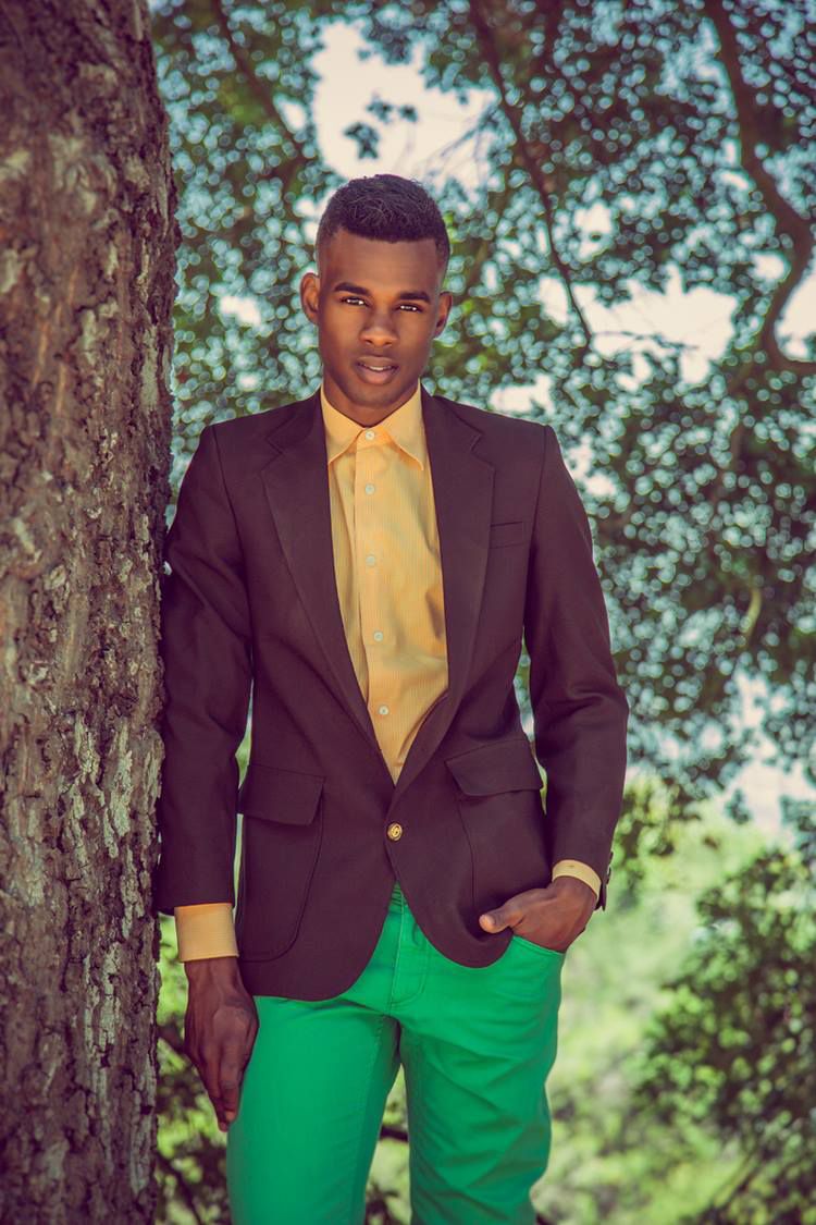 Stylish portrait featuring brown blazer, yellow shirt and green pants against tree background.