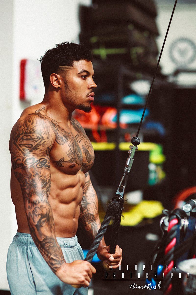 Tattooed fitness model exercising with cable machine in gym setting.