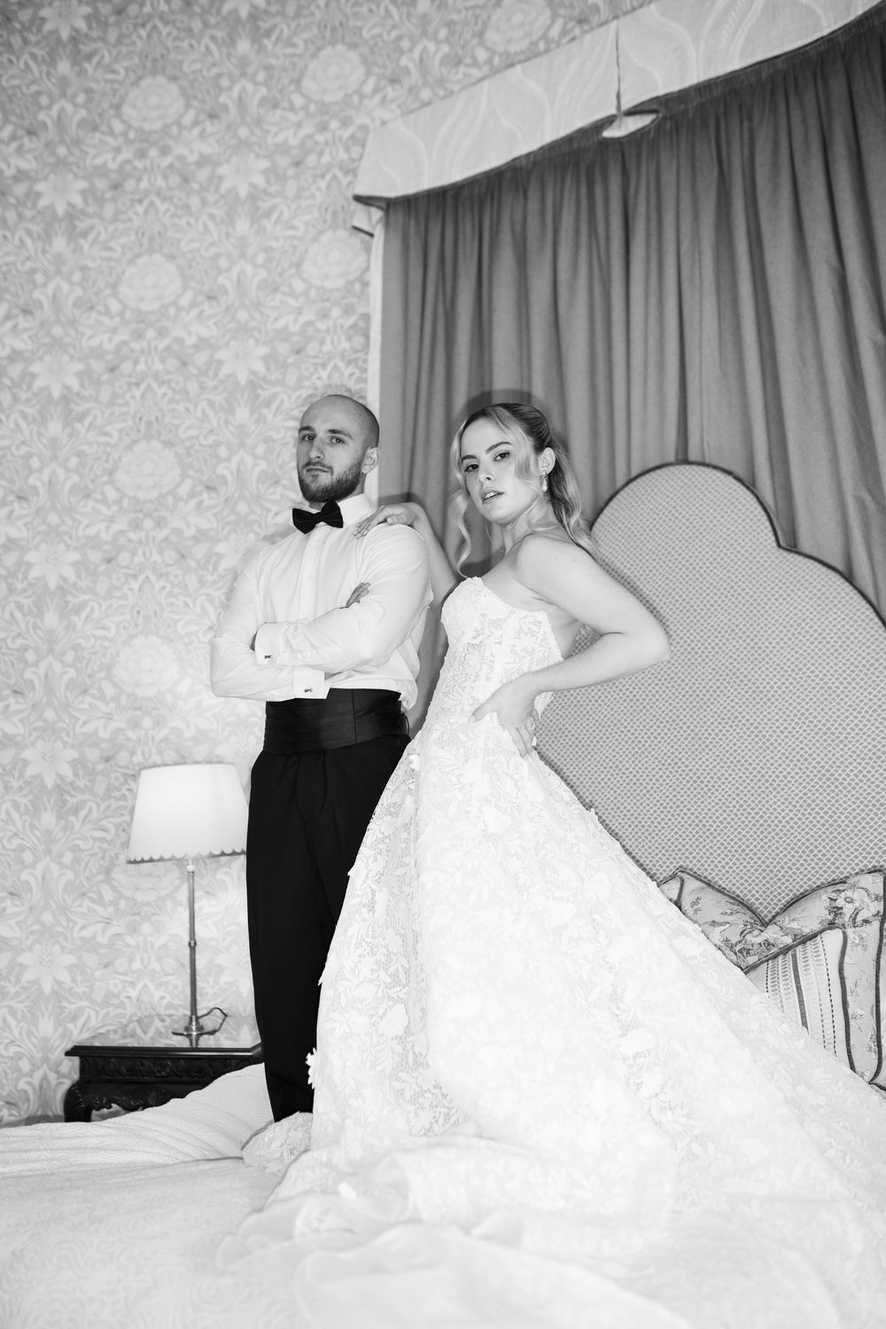 Black and white wedding photos show a sequence of romantic poses on a couch with floral wallpaper and elegant drapery.