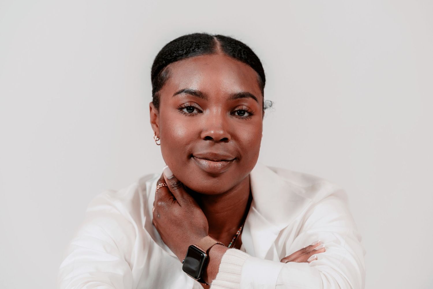 Professional portrait against light gray background showing person wearing white button-down shirt and smart watch.