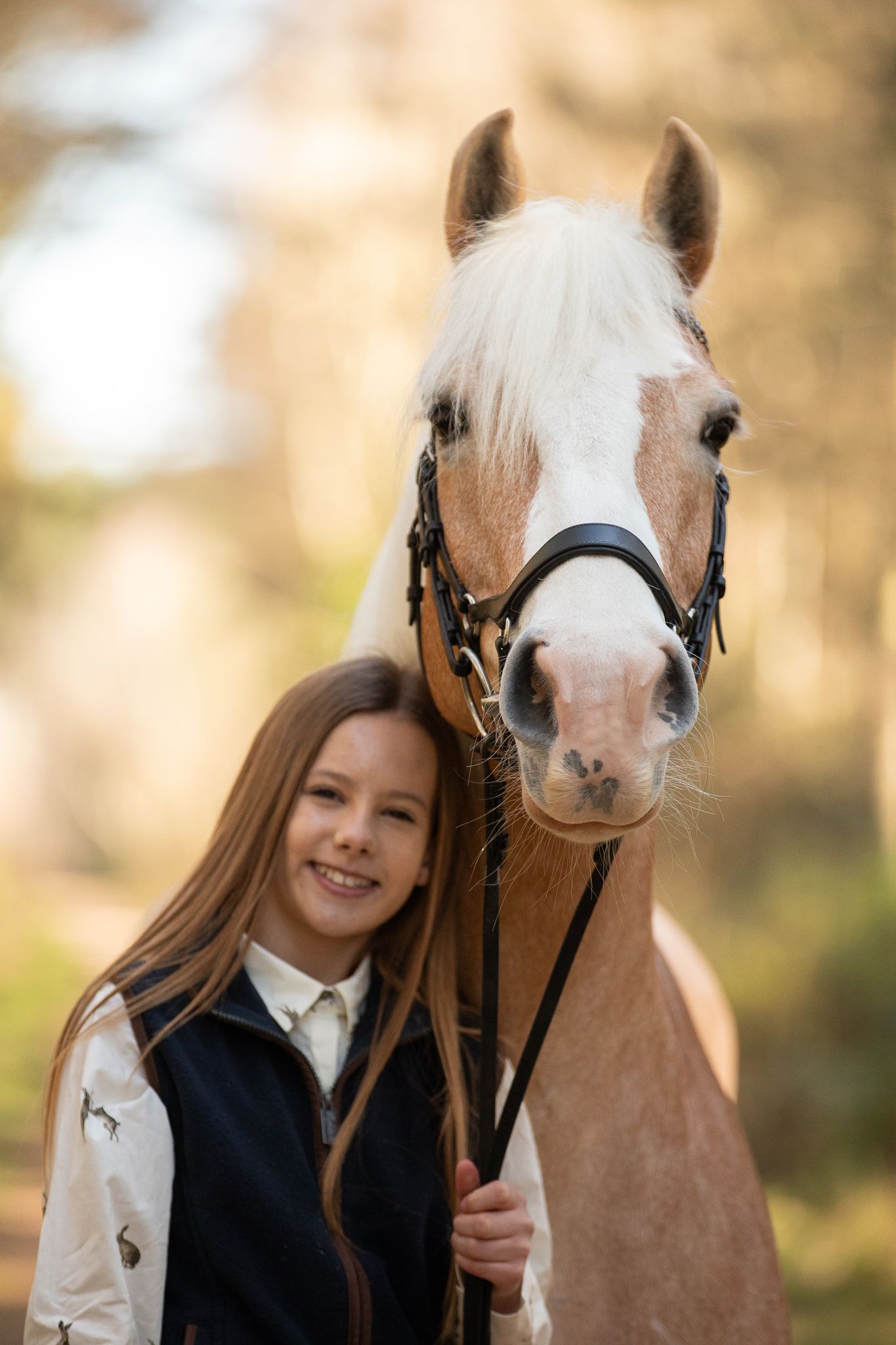 Young equestrian poses with palomino pony in a series of natural outdoor portraits showing their special bond.