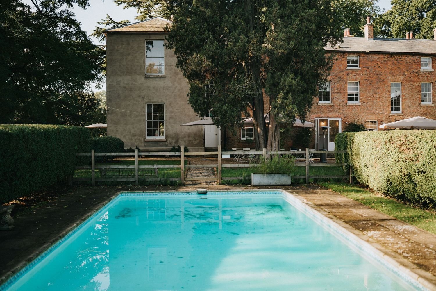A backyard with a turquoise swimming pool and brick buildings surrounded by trees at Aswarby Rectory - taken by Grimsby photographer.