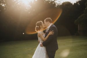A couple in wedding attire embracing in a sunlit garden during golden hour sunset at Cave Castle - taken by Grimsby photographer.