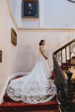 A bride in a lace wedding gown with long white train poses on red carpeted stairs at Cave Castle - taken by Grimsby photographer.