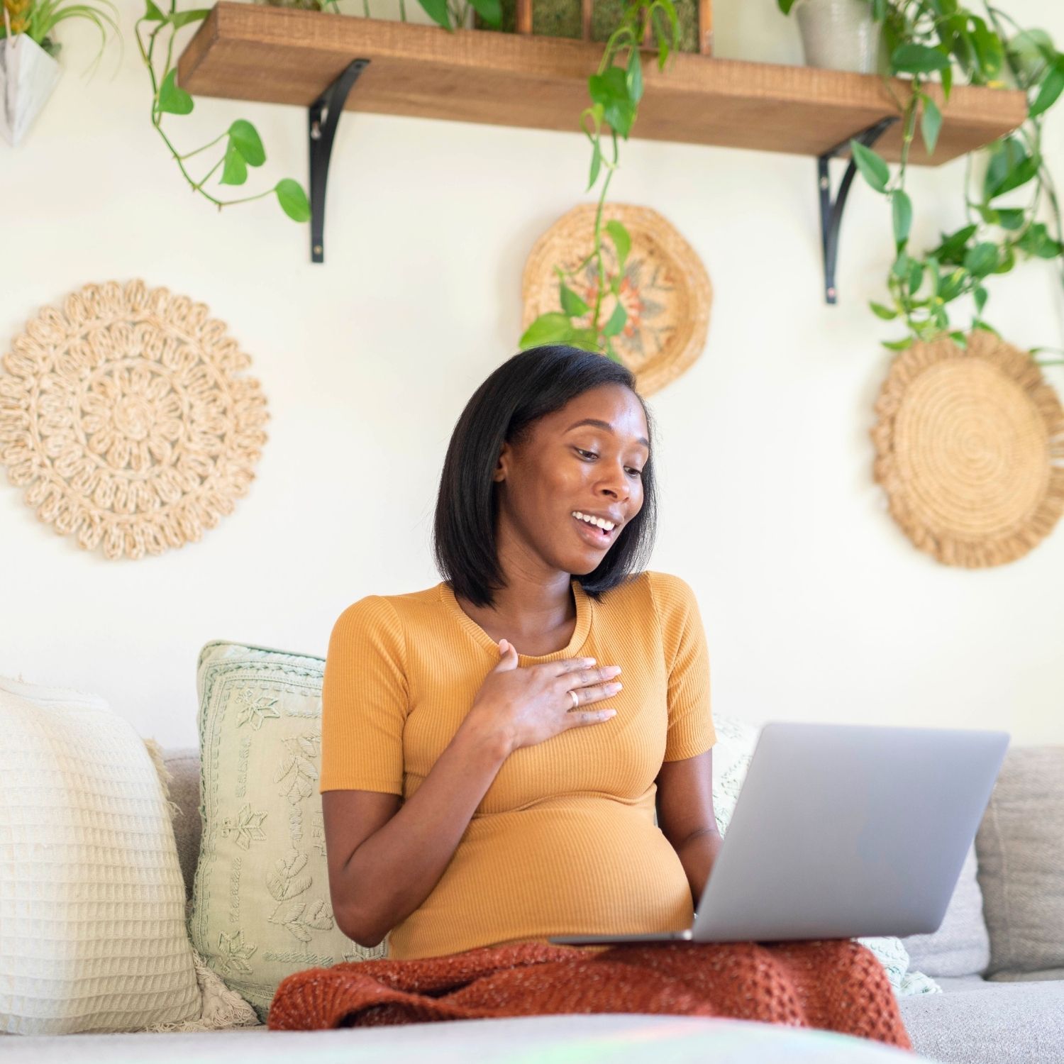 Pregnant woman dressed in a yellow shirt smiling and looking at het laptop as she had seen something adorable.