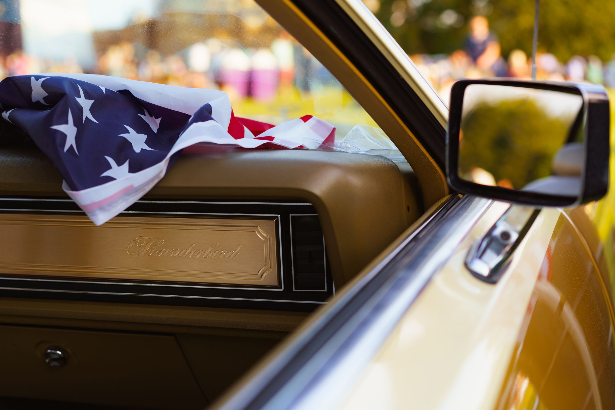 Shot of the dashboard of a vintage, gold Thunderbird car with an American flag on the dashboard, shot from outside the window