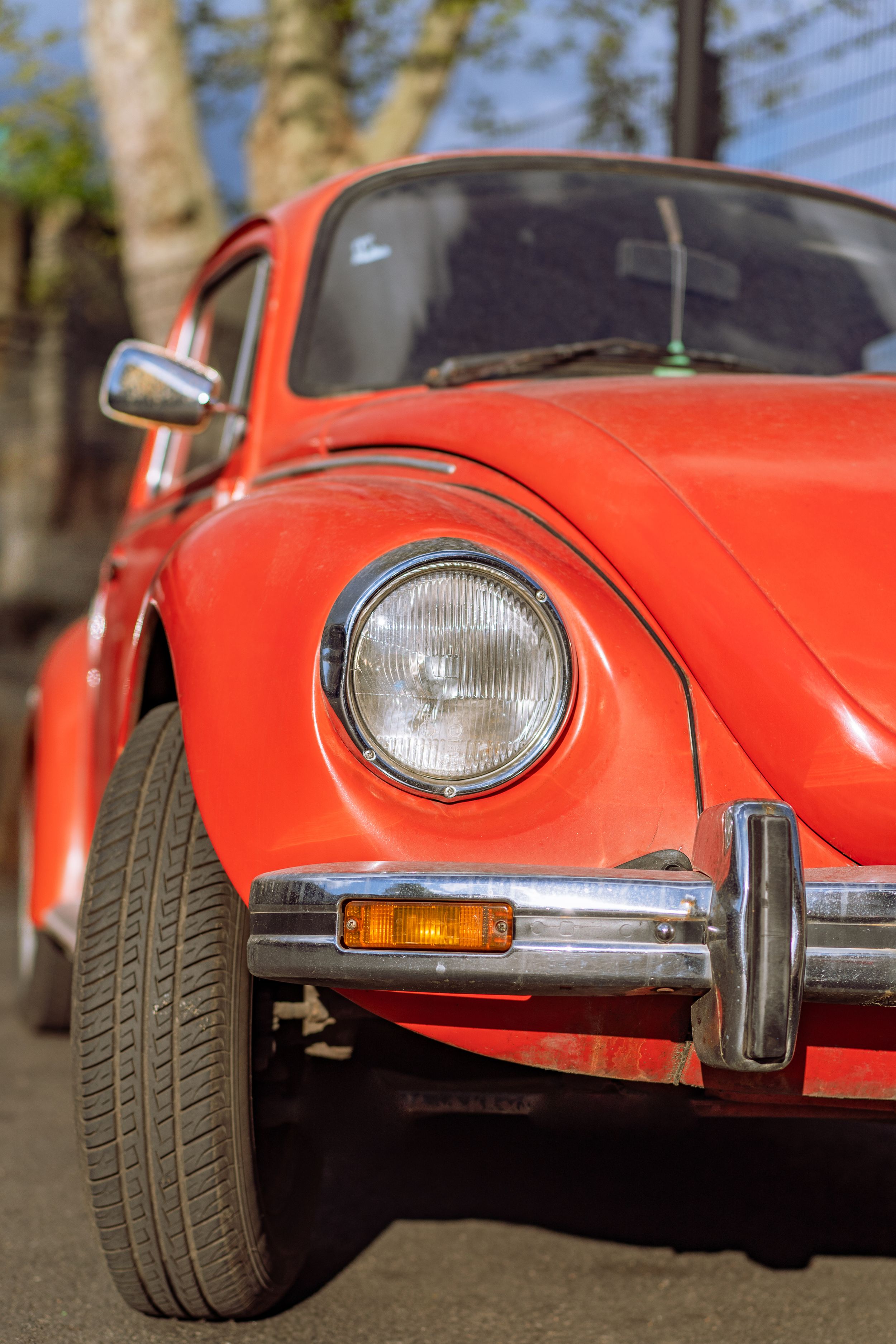 A red-orange VW Beetle car's right headlight from the front with the front wheel turned outwards