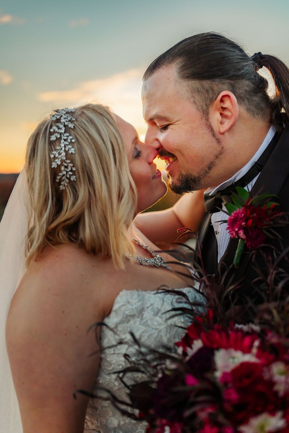 A romantic couple shares intimate kisses at sunset with deep red flowers in the foreground.