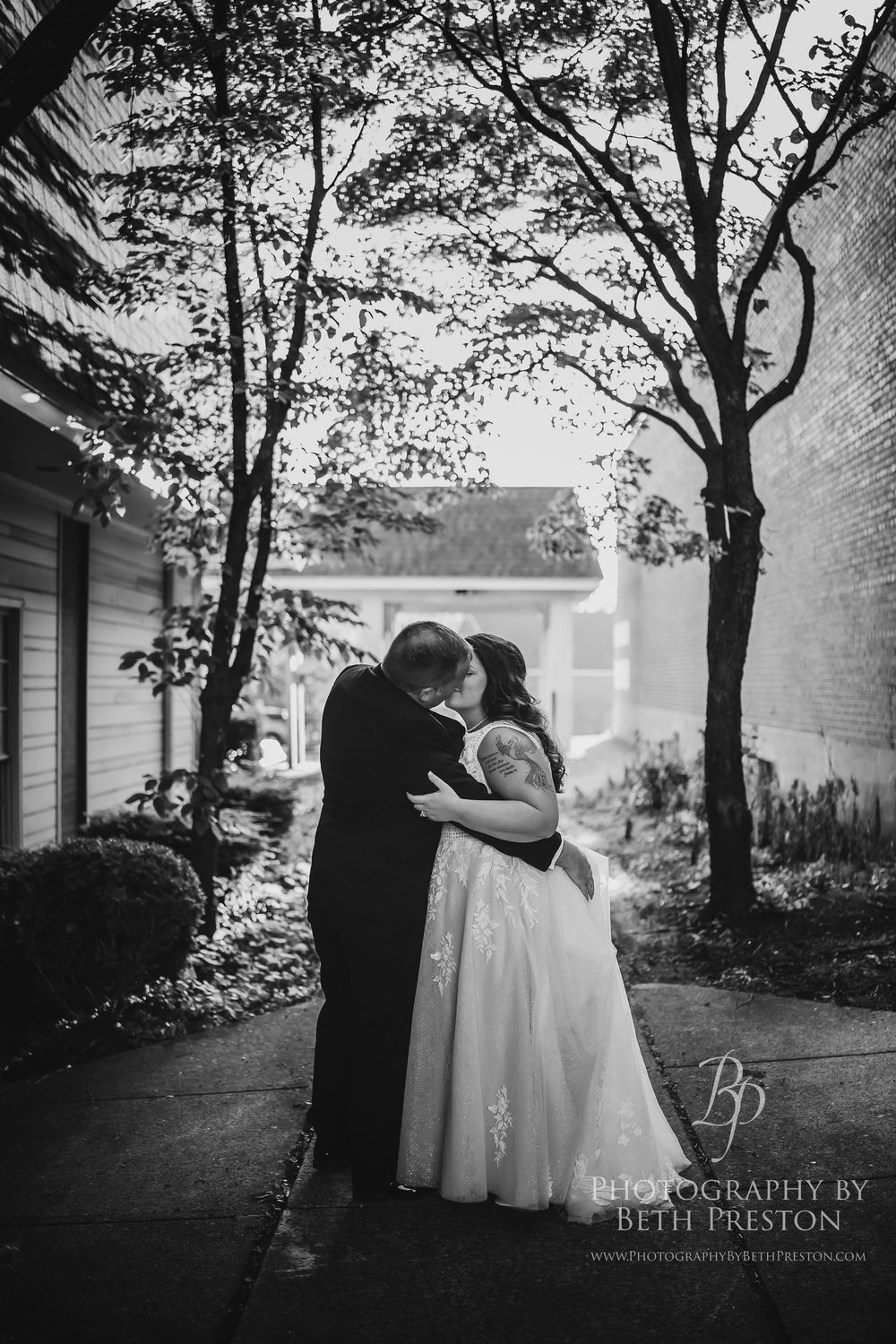 Black and white romantic wedding photos show couple embracing under tree-lined path with natural lighting and soft shadows.