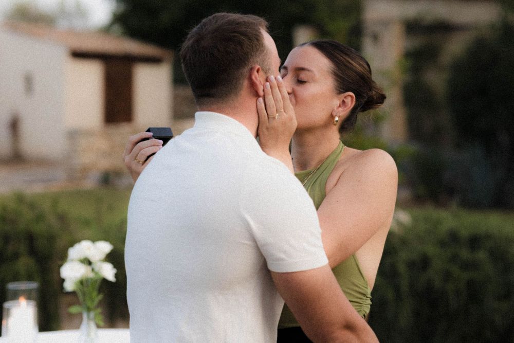 Couple embracing in a tender kiss after proposal with white flowers on table.