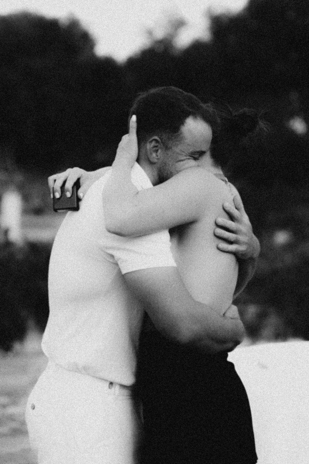 A black and white photo of an intimate embrace between two people sharing a tender moment outdoors.
