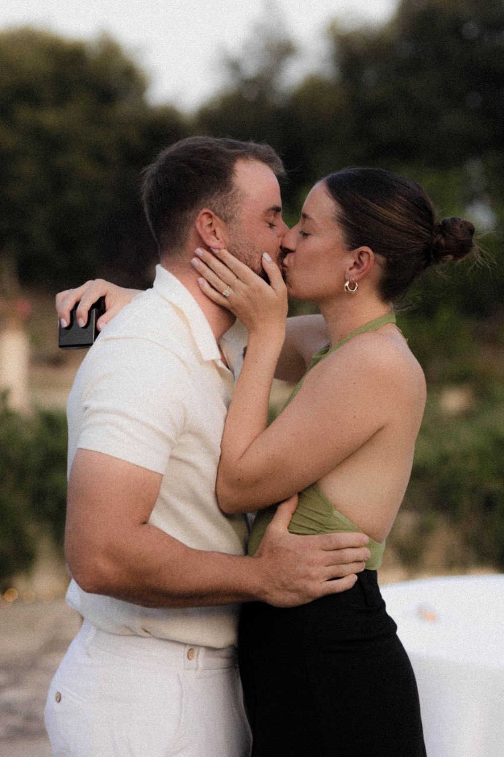 Couple shares tender moment in white and black outfits against outdoor backdrop.