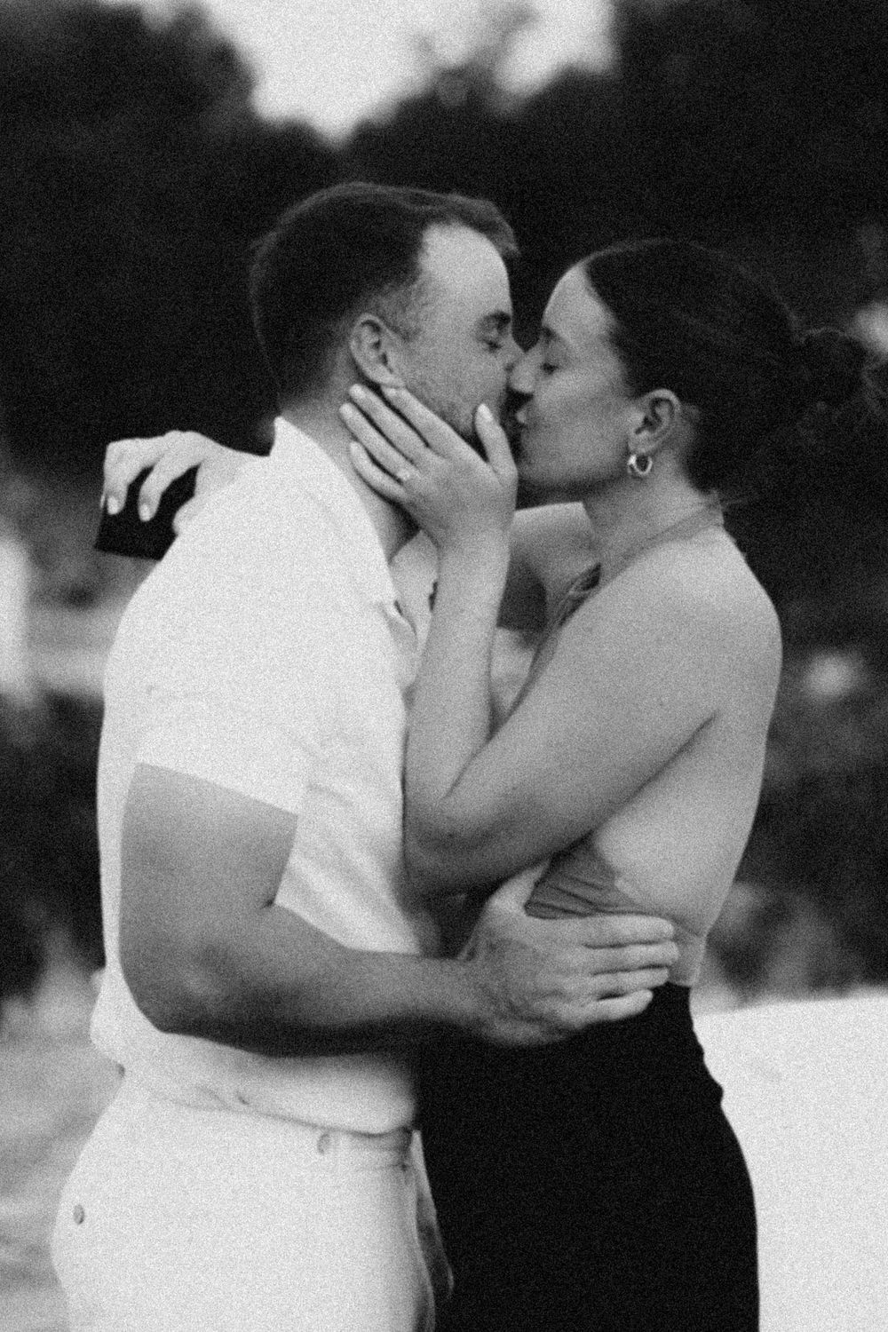 A romantic black and white photograph showing a couple sharing an intimate kiss outdoors.