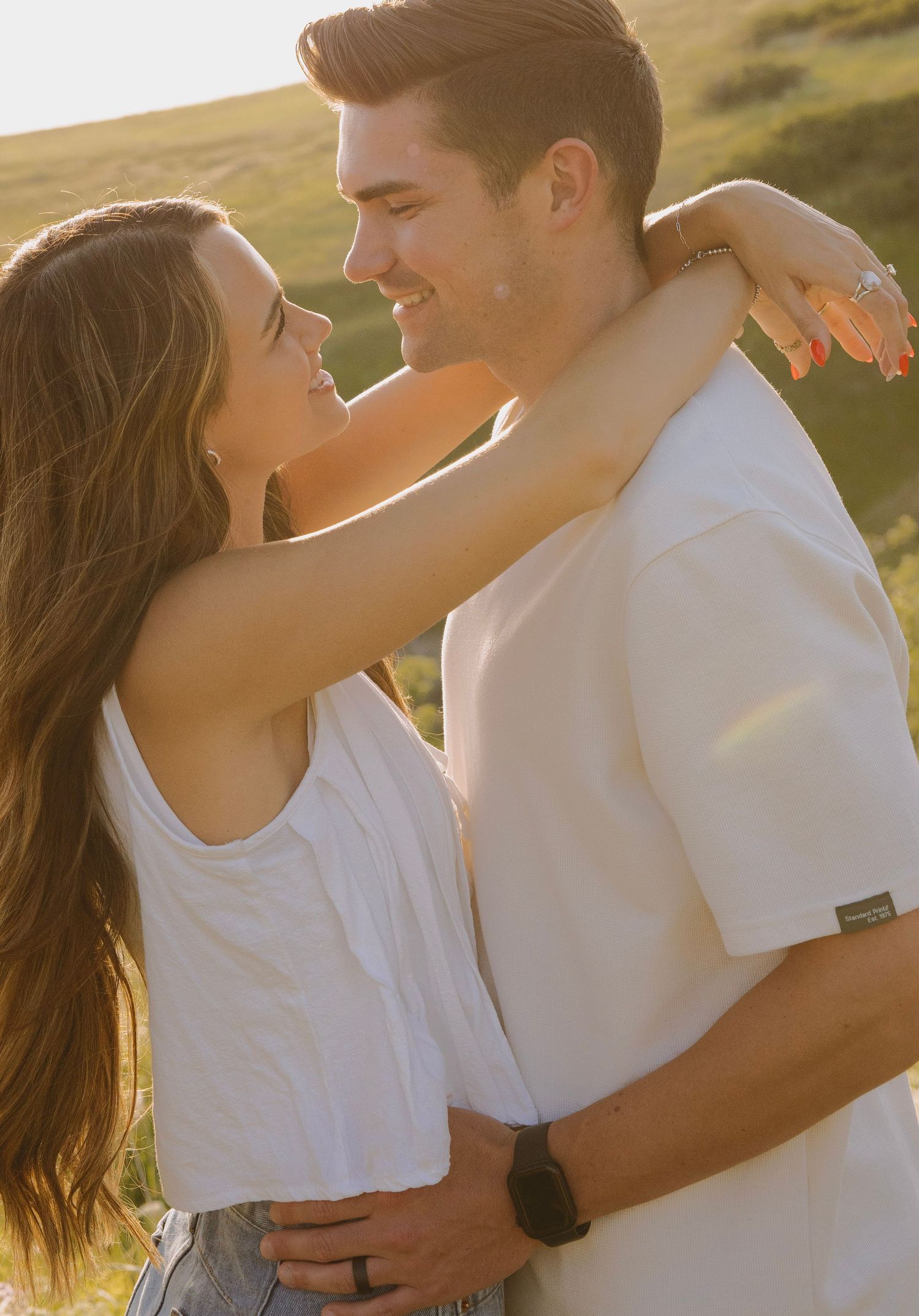 Two people embrace in white outfits while standing on red rock formations in a desert canyon landscape.
