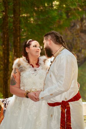 A romantic forest wedding scene with a couple in traditional white and red ceremonial attire.