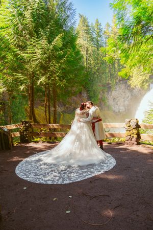 A beautiful lace wedding gown with a long flowing train spreads elegantly across a forest path in natural lighting.