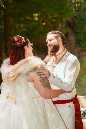 Couple in renaissance-style wedding attire embraces romantically among forest trees.