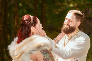 A joyful wedding moment captured in a sunlit forest setting with traditional white and fur attire.
