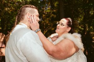 A tender moment between newlyweds in matching white outfits against a natural outdoor backdrop.
