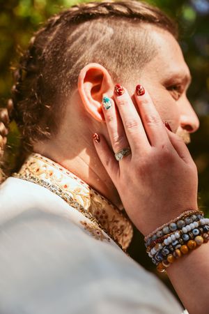 A close-up profile view showing painted nails and layered beaded bracelets during a wedding celebration.