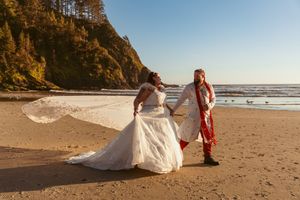 Beautiful coastal wedding photography session at sunset with bride's flowing dress on a sandy beach against cliffs.