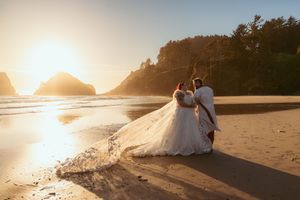 Romantic sunset beach wedding photos with silhouettes against warm orange sky and rocky coastline.