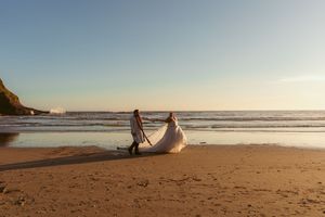A couple walking along a scenic beach at sunset with their wedding attire flowing in the breeze.