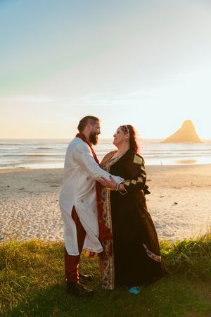 A couple shares a loving moment on a beach at sunset wearing ethnic-inspired ceremonial dress.