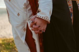 Close up of a couple holding hands showing detailed white sleeves and wedding attire.