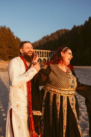Couple dressed in medieval-inspired wedding attire share laughter against winter landscape.