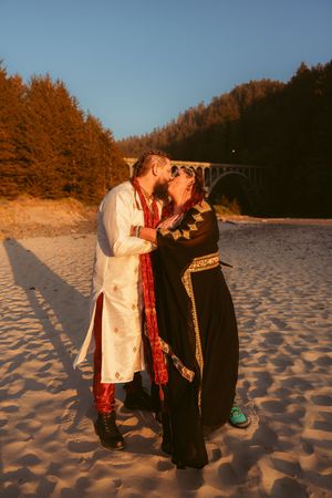 A couple in traditional Indian wedding attire sharing an intimate moment on a beach at golden hour.