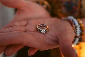A diamond engagement ring rests in an outstretched palm adorned with beaded bracelets.