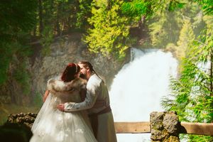 A wedding couple share an intimate moment in front of a majestic waterfall surrounded by lush greenery.