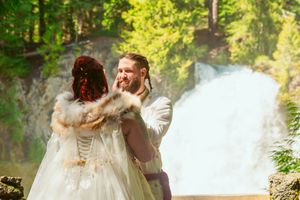 A couple in wedding attire embracing in front of a majestic waterfall.