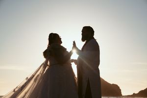Silhouettes of a couple in wedding attire embrace against a misty coastal backdrop at dusk.