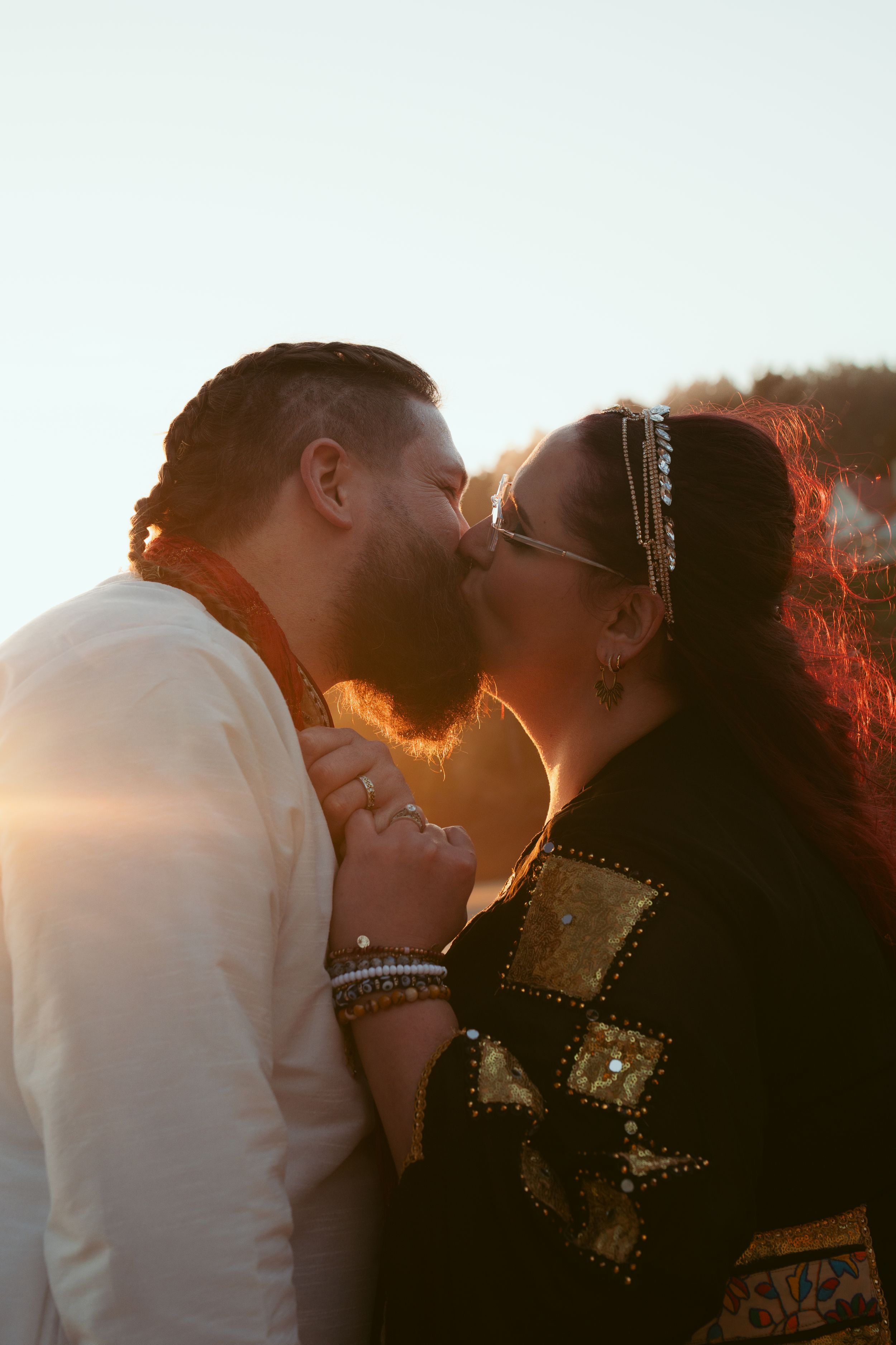 A romantic sunset silhouette shows a couple sharing an intimate moment while wearing traditional attire.