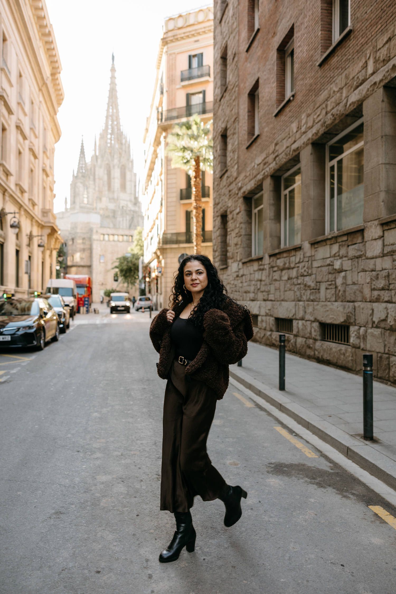 Woman in dark winter coat poses dramatically on European city street with cathedral view.