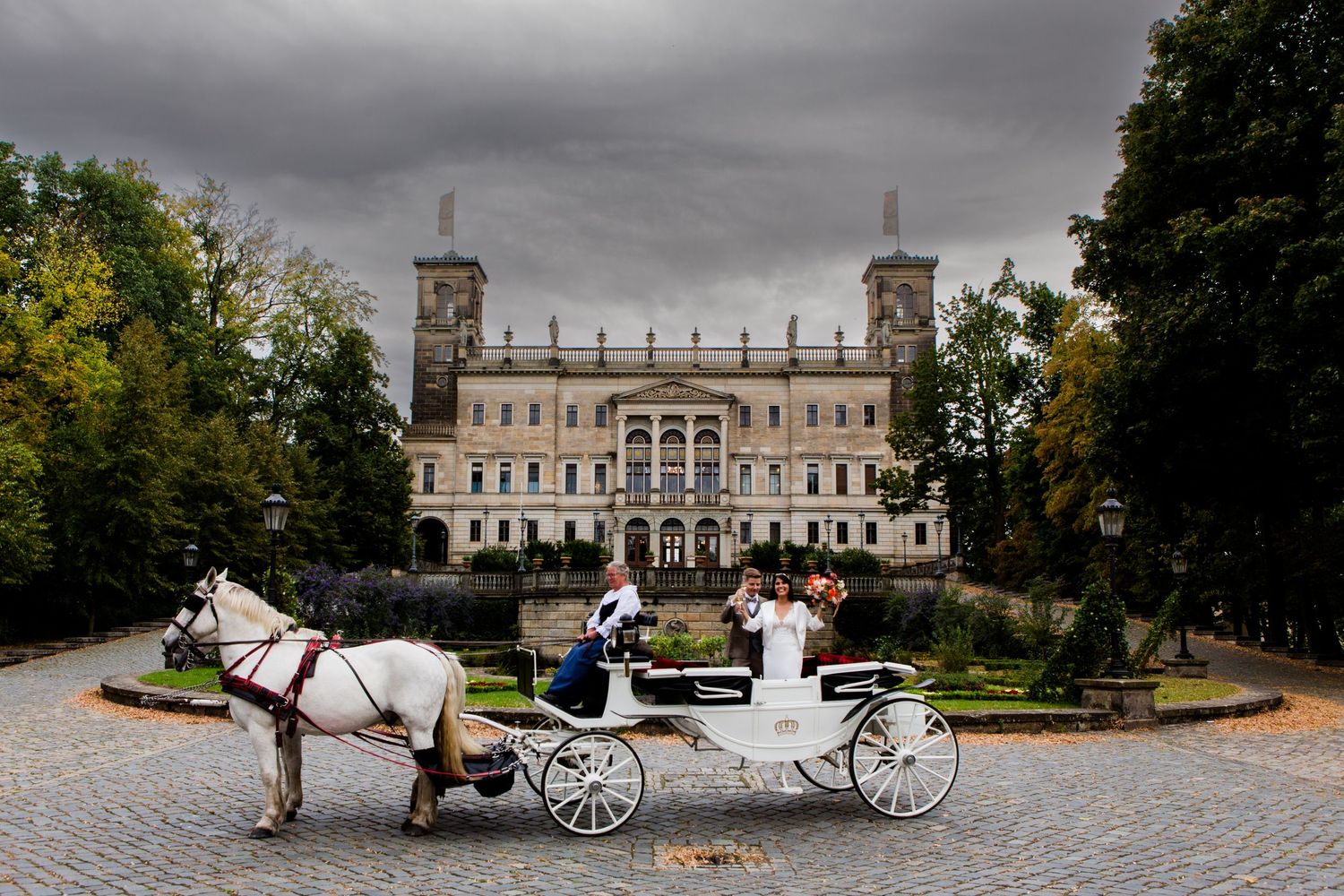 A white horse-drawn carriage waits in front of a grand palace with twin towers under dramatic stormy skies.