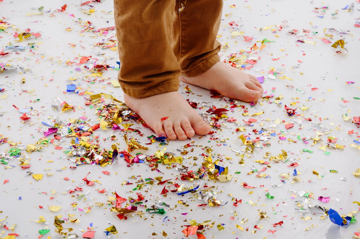 Detail shots of feet walking through colorful confetti scattered on white floor.