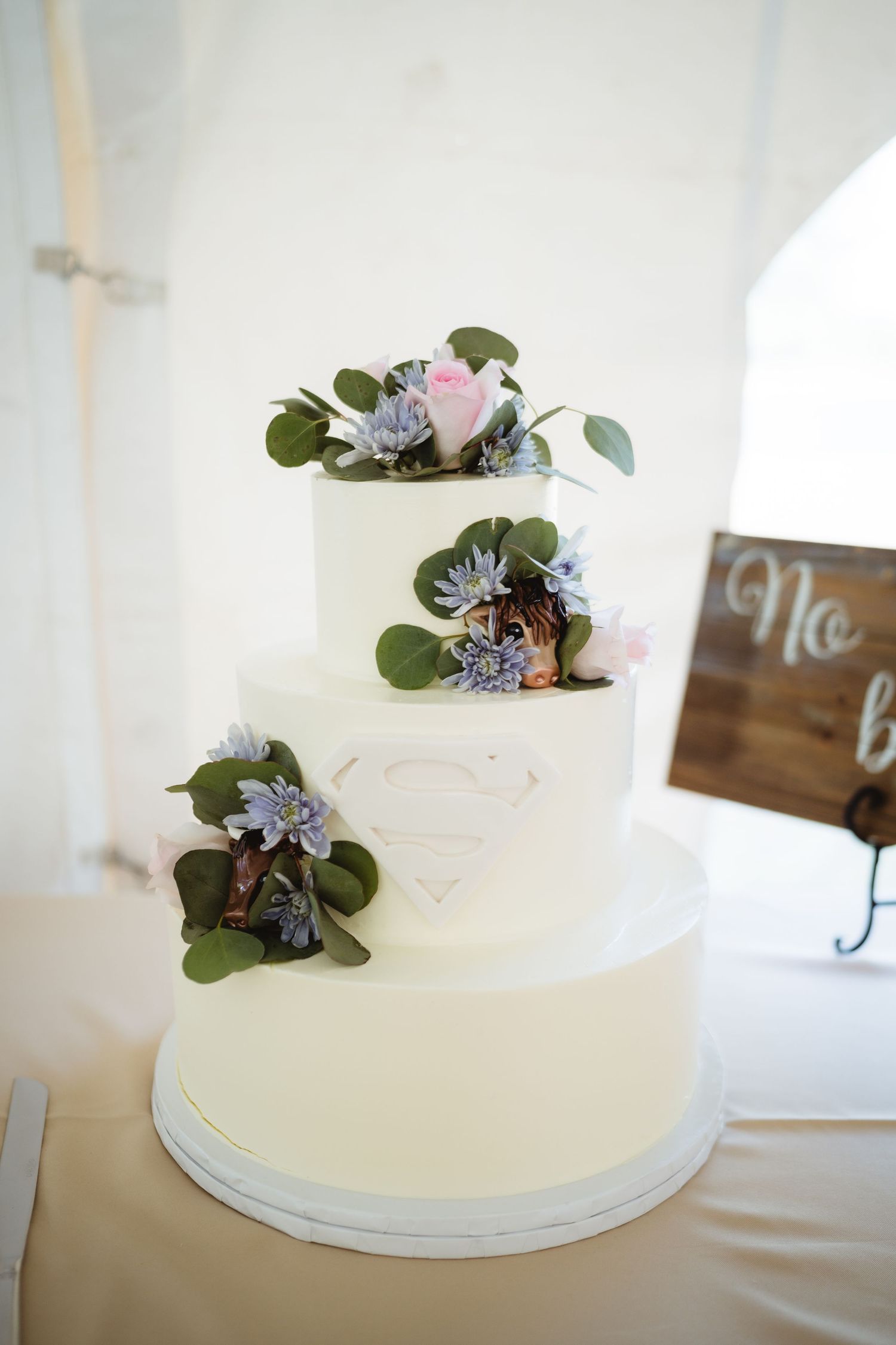 A white buttercream wedding cake adorned with small purple flowers and eucalyptus leaves shown from different angles.