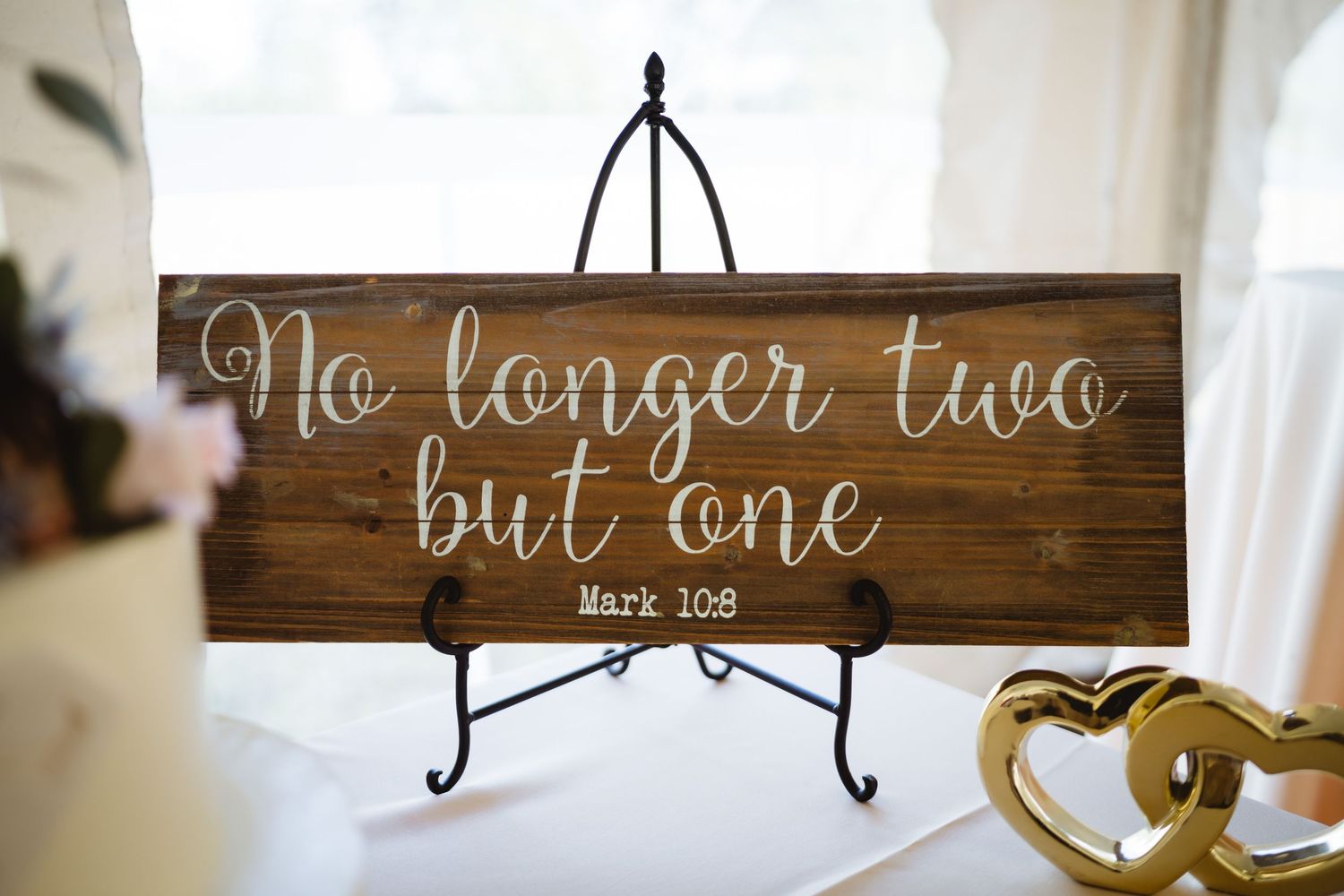 Dark wooden signs with white calligraphy text displayed on iron easels for a wedding celebration.