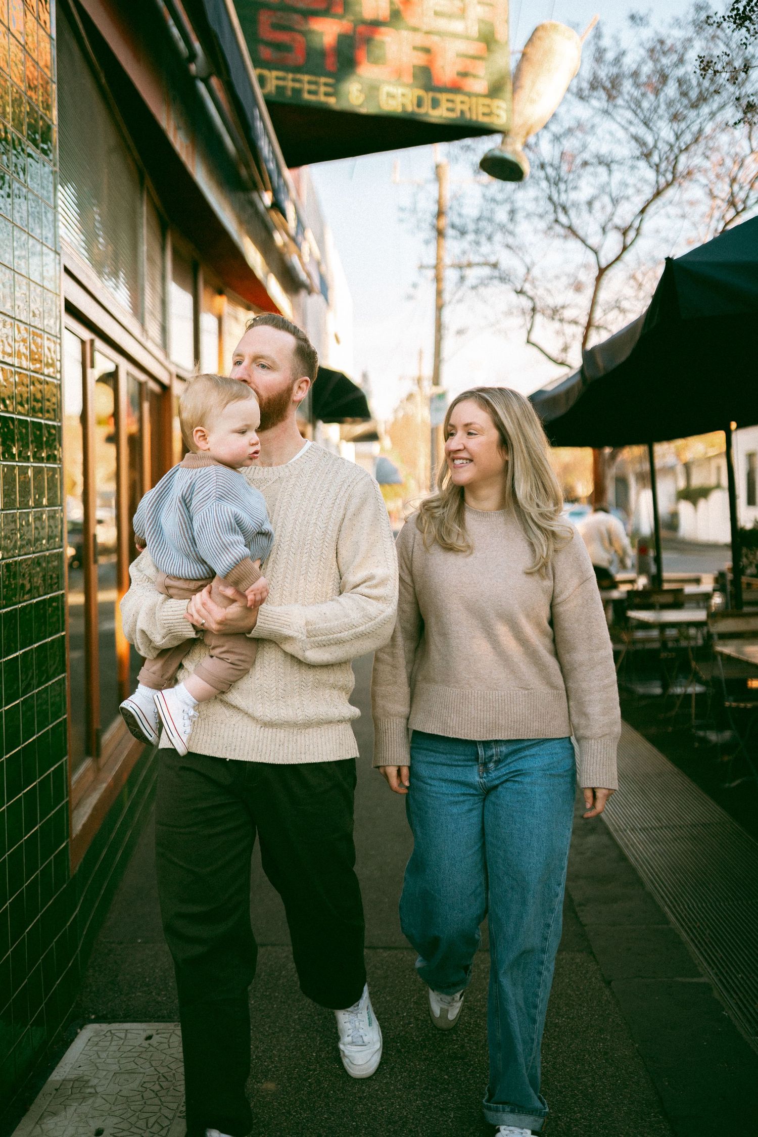 Family walking past a café in Richmond during a documentary-style neighbourhood photo session, with parents chatting and baby in arms.