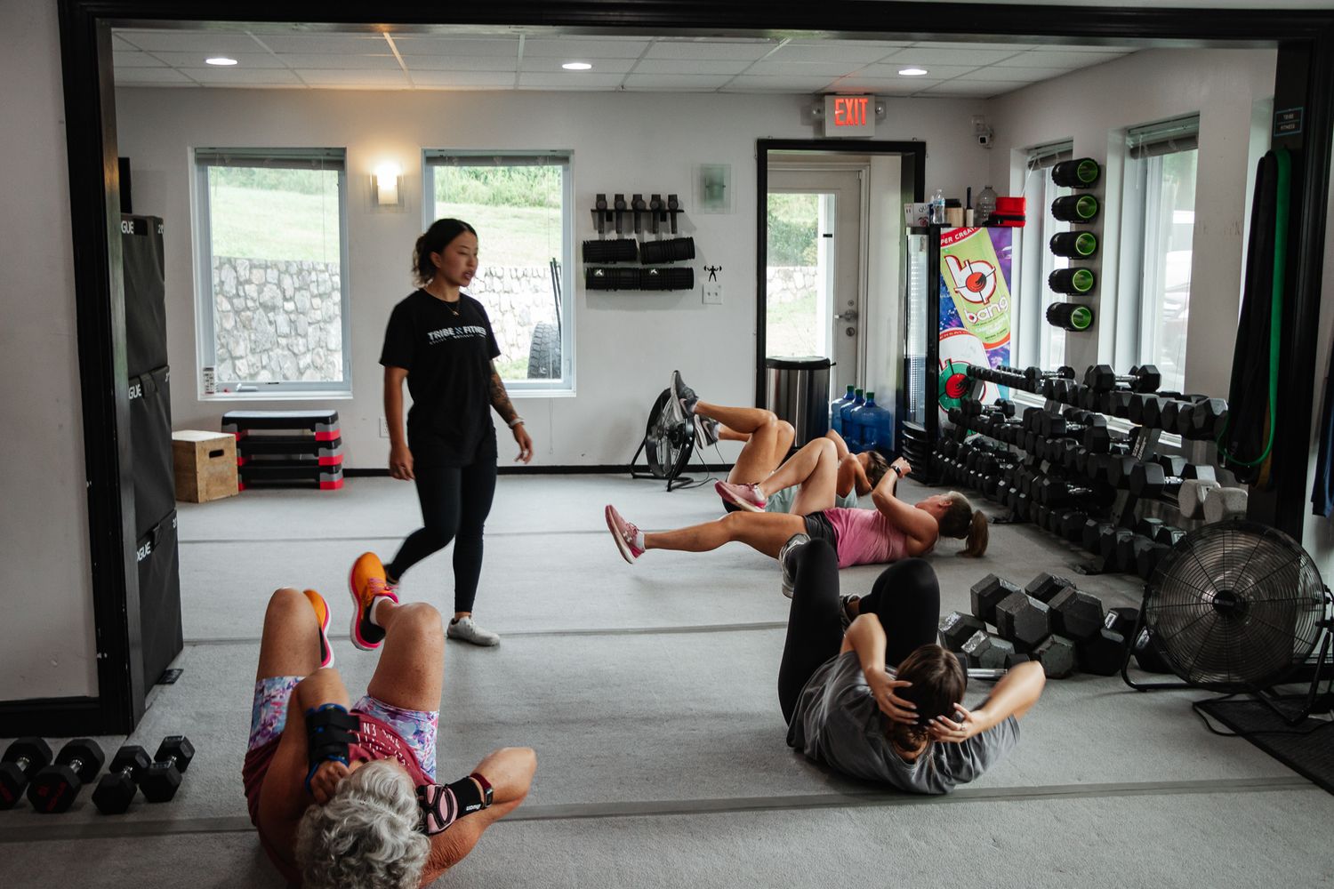 Fitness instructor walks around a gym as participants perform bicycle crunches on the floor