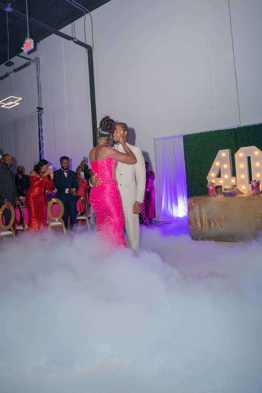 Couple dancing on a misty dance floor with pink lights and decorative number 40 visible in the background.