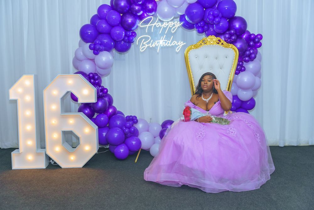 Lavender and purple balloon decorations arranged in an elegant display against a white backdrop for a special event.