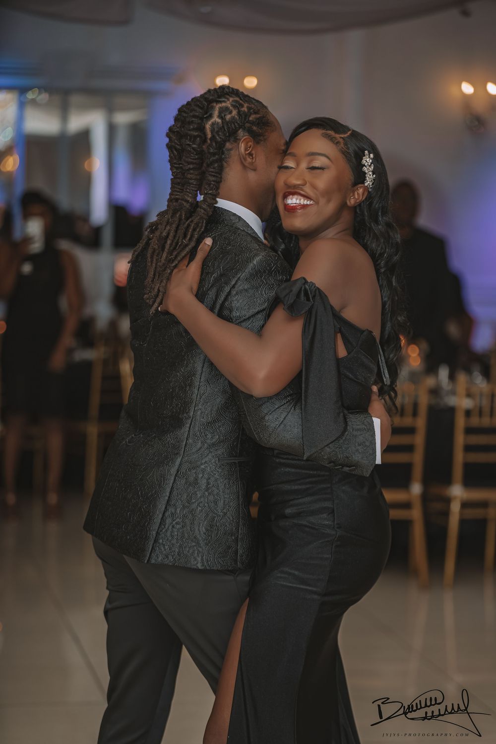 A couple shares a joyful dance moment at an elegant indoor reception with soft lighting and ambient decor.