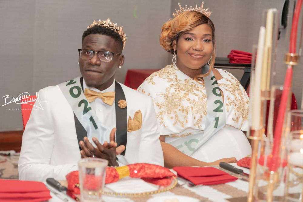 Two people dressed in elegant white and gold attire sit at a formal dinner table with red accents.