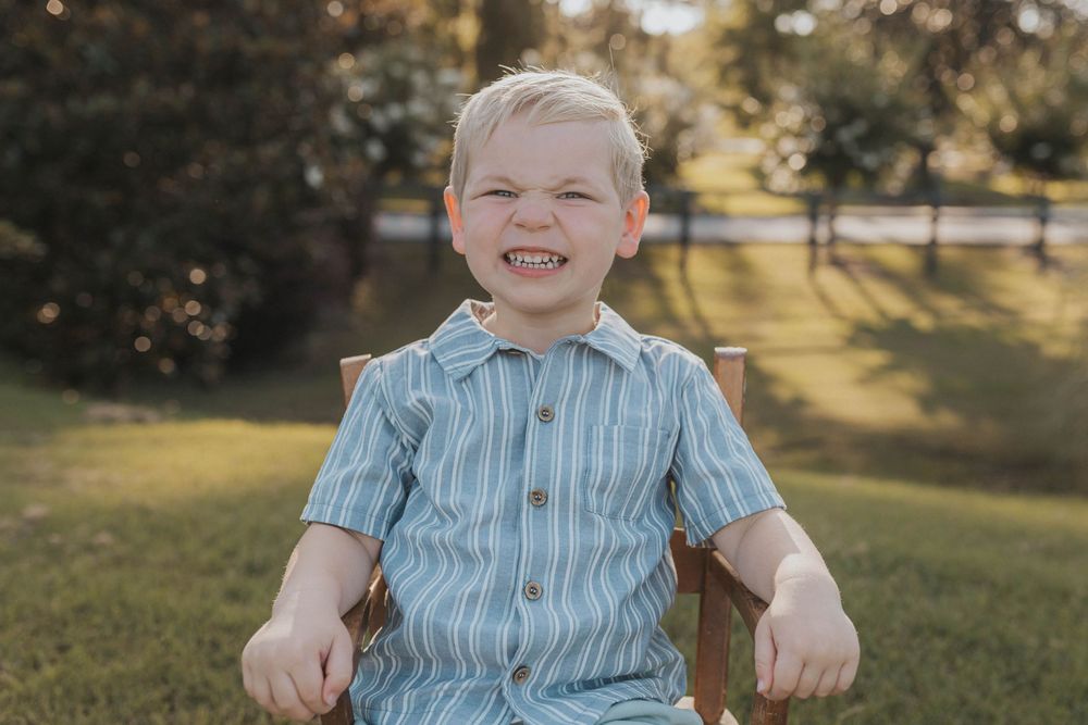 A child in a striped blue shirt smiles brightly while sitting outdoors.